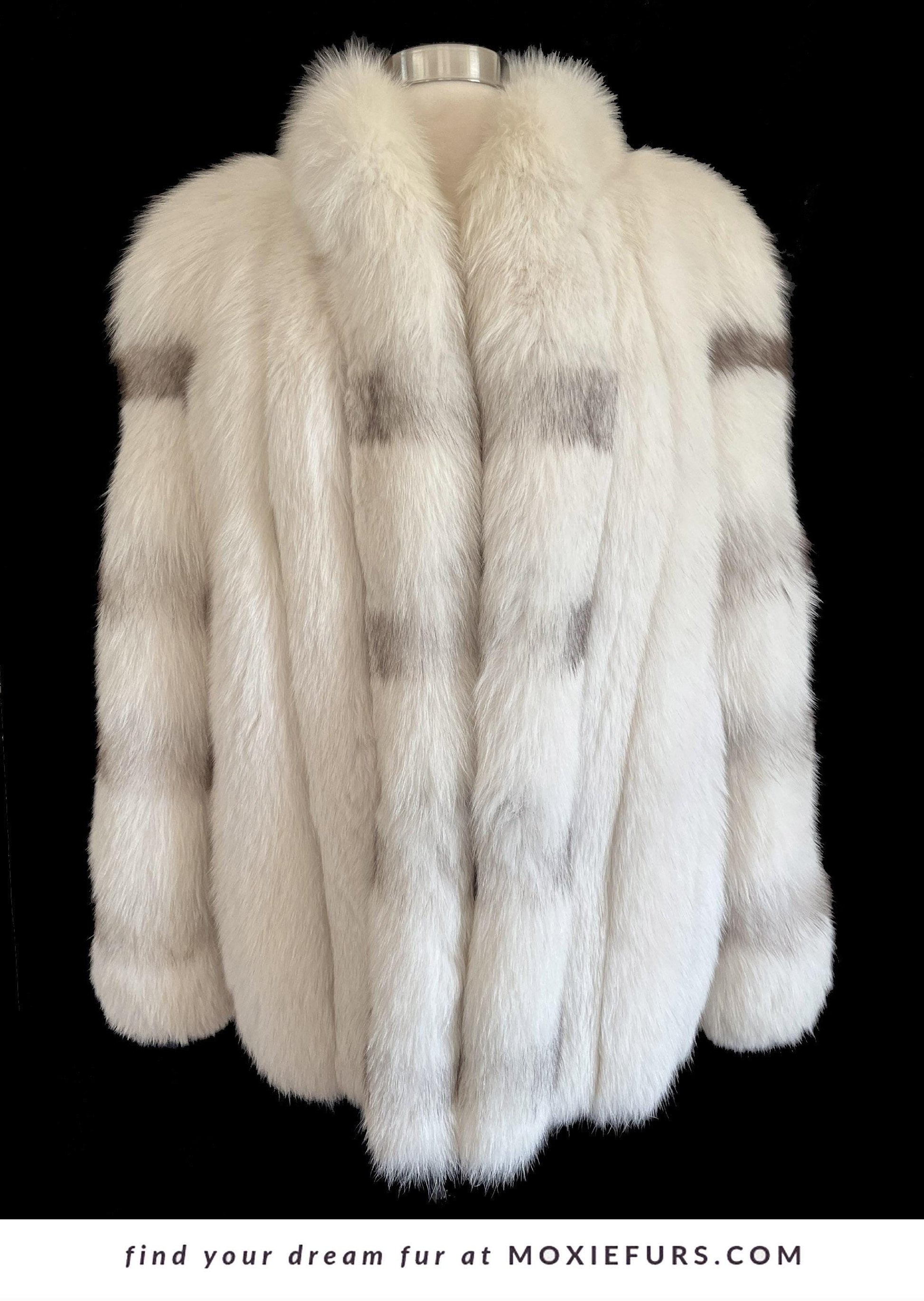 May include: A luxurious white fur coat with gray accents. The coat features a wide collar and a soft, textured appearance. The image includes the text "find your dream fur at MOXIEFURS.COM".
