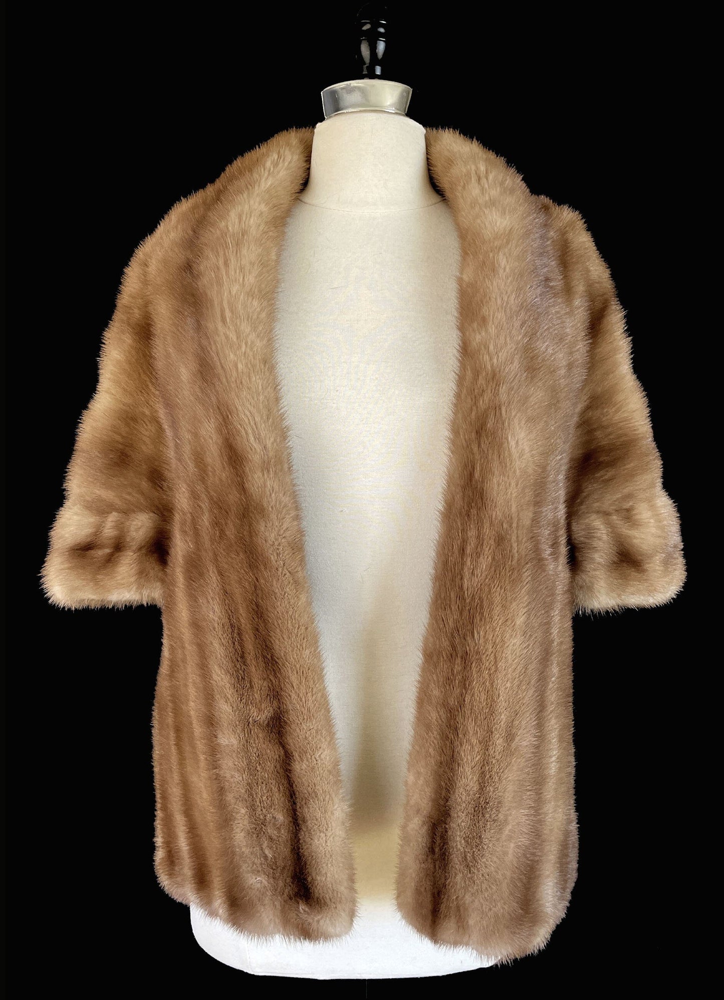 May include: A light brown fur coat with short sleeves is displayed on a mannequin against a black background. The coat has a wide collar and a soft, luxurious texture. The text "find your dream fur at MOXIEFURS.COM" is at the bottom.