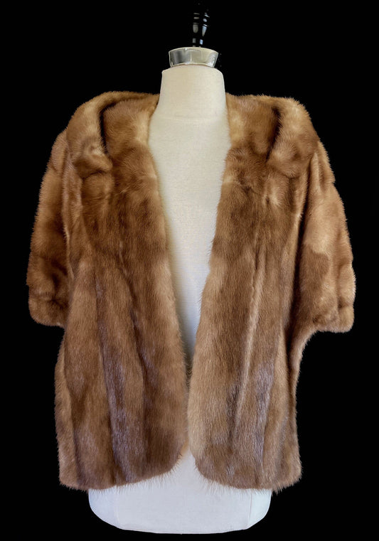 May include: A brown fur jacket with short sleeves displayed on a mannequin against a black background. The jacket has a soft, textured appearance. The text "find your dream fur at MOXIEFURS.COM" is at the bottom.
